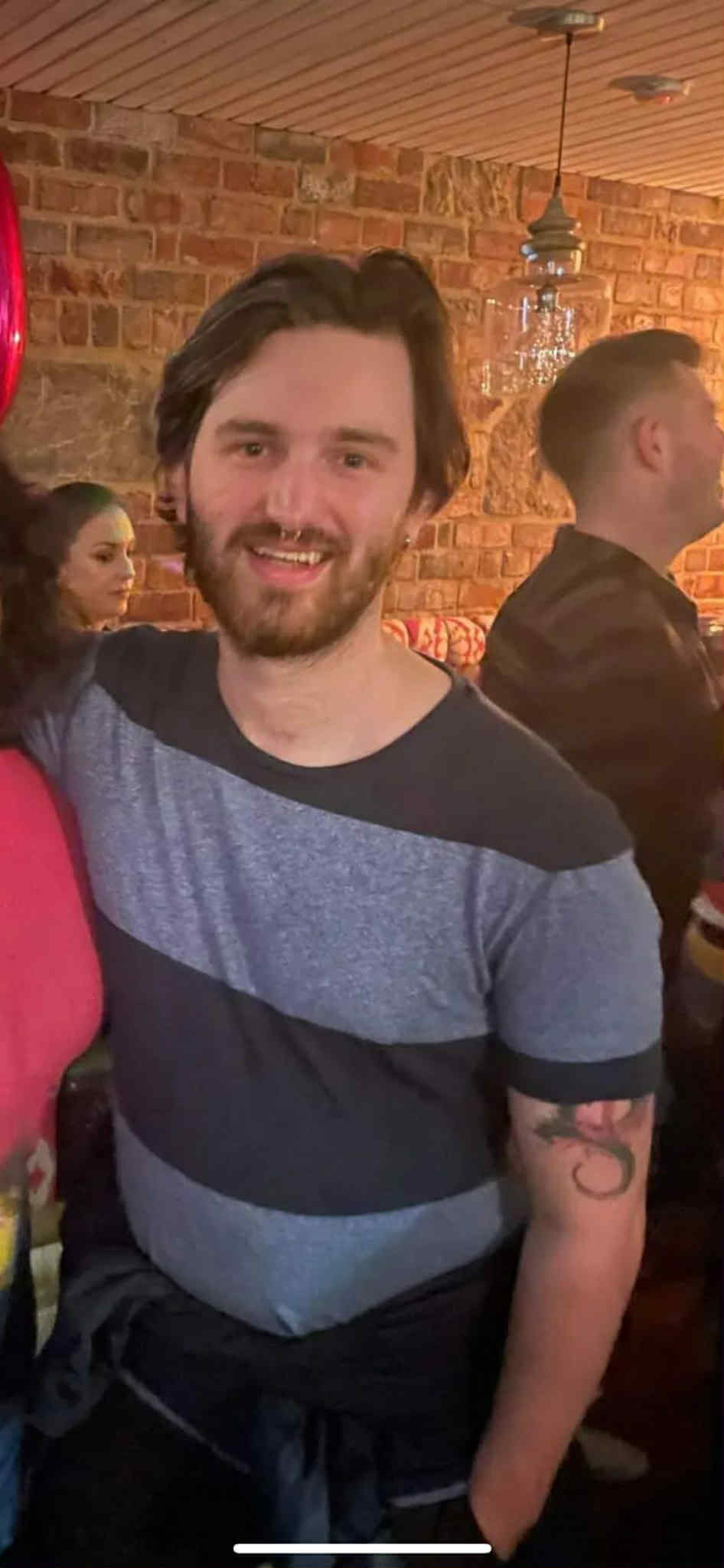 Mark standing in a social setting with brick wall background