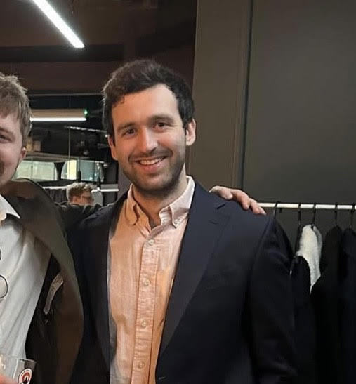 Jamie dressed in a suit standing beside friend in a social setting.